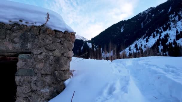雪の山の中に放棄された石造りの小屋 元刑務所だ 針葉樹林と日没 雪がたくさん 古代の石の壁 入口へと続く道 雲は遠くに見える — ストック動画