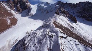 Dağlarda eski bir kar buzulu. Yukarıdan, karla kaplı dik uçurumlardaki bir dronun görüntüsü. Bir buzulla kaplı yüksek zirveler. Bazı yerlerde büyük taşlar var. İzler görünüyor.