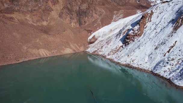 エメラルド水のある山の湖は鏡のような氷河を反映しています 山の峰が見えます 湖は部分的に凍結されている 場所には大きな石や雪があります モレーン湖 — ストック動画