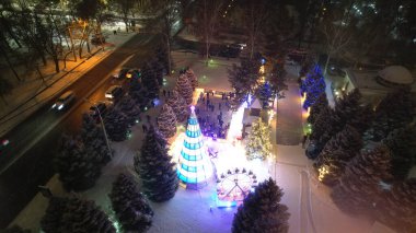 Noel ağacıyla süslenmiş parlak Noel süslemeleri. Noel ağacında çelenkler ve neon oyuncaklar parlıyor. Noel ve Yeni Yıl için dekorasyon. Kar yağıyor. İnsanlar fotoğraf çeker. İHA 'dan üst görünüm