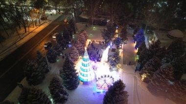 Noel ağacıyla süslenmiş parlak Noel süslemeleri. Noel ağacında çelenkler ve neon oyuncaklar parlıyor. Noel ve Yeni Yıl için dekorasyon. Kar yağıyor. İnsanlar fotoğraf çeker. İHA 'dan üst görünüm