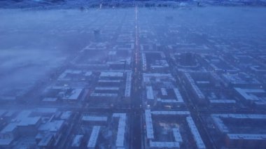 Dawn over the city in fog and smog. Mountain view. A light haze hangs over the city, cars drive, signs glow. Clouds, sun rays and snowy mountains are visible in the distance. Almaty, Kazakhstan