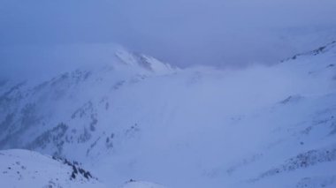 Karlı dağlarda bulutların olduğu mistik şafak. Beyaz tepeler bulutlar ve karla kaplıdır. Dik kayalıklar. Zirvenin zirveleri. Şafak vakti güneş ışınları bulutların arasından geçer.
