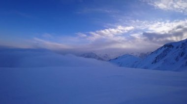 A timelapse of an ocean of clouds in the mountains. White clouds are like a carpet in the gorge. Waves rise and descend from the mountains. Everything is covered in snow. Sunrise of the yellow sun