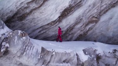 A climber walks on a large glacier in the mountains. A high frozen wall of ice similar to marble. Unusual coloring is gray-white with streaks. The glacier is collapsing. Lots of snow. Blue sky. Almaty