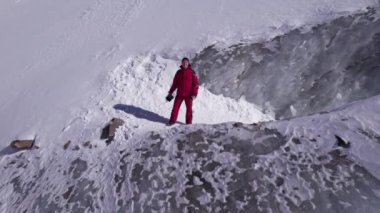 The guy in red is standing on top of the glacier. Frozen moraine lake in the mountains. Lots of snow. Aerial view from a drone of people, mountains and trails in the snow. The ice is breaking down