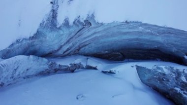A huge ice wall from a glacier in the mountains. Everything is covered with snow and large stones. Top view from the drone on the cracks in the ice. The glacier breaks, the ice flakes off. Almaty