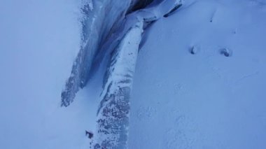 A huge ice wall from a glacier in the mountains. Everything is covered with snow and large stones. Top view from the drone on the cracks in the ice. The glacier breaks, the ice flakes off. Almaty