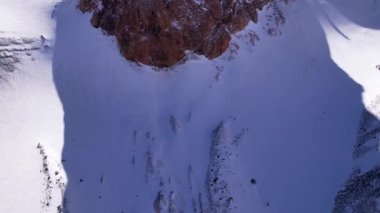 High snow-capped mountains among glaciers. Aerial view from a drone on a rocky gorge. The glacier is covered with snow and rocks. The sky is blue and the sun is shining brightly. The ice is cracking