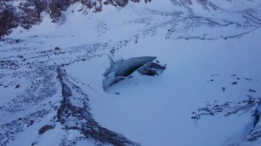 A huge ice wall from a glacier in the mountains. Everything is covered with snow and large stones. Top view from the drone on the cracks in the ice. The glacier breaks, the ice flakes off. Almaty