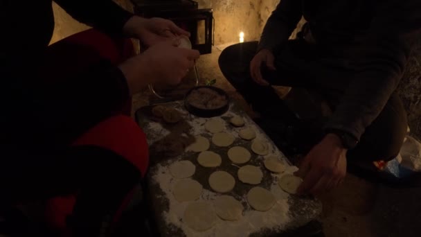 在一个古老的小屋里做饭 他们做饺子 一间废弃的茅屋里温暖的气氛 营房的炉灶和蜡烛生着火 游客在野营桌上做饺子 油锅中的切肉 — 图库视频影像