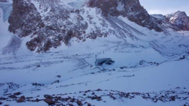 A huge ice wall from a glacier in the mountains. Everything is covered with snow and large stones. Top view from the drone on the cracks in the ice. The glacier breaks, the ice flakes off. Almaty