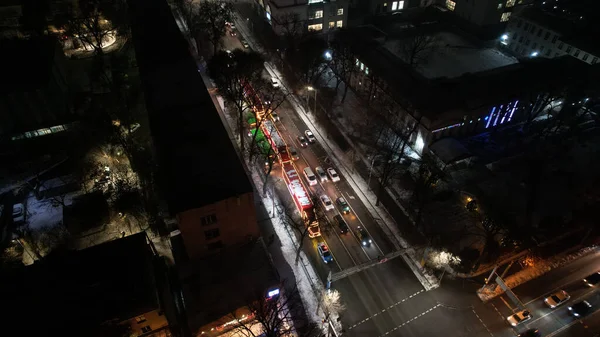 Red big trucks with Coca Cola drive through the streets of the city. Average traffic of cars. Lights and headlights are shining. New Years mood. Top view from the drone on the houses and the road