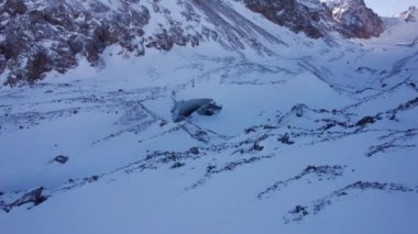 A huge ice wall from a glacier in the mountains. Everything is covered with snow and large stones. Top view from the drone on the cracks in the ice. The glacier breaks, the ice flakes off. Almaty