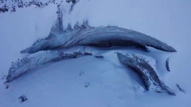 A huge ice wall from a glacier in the mountains. Everything is covered with snow and large stones. Top view from the drone on the cracks in the ice. The glacier breaks, the ice flakes off. Almaty