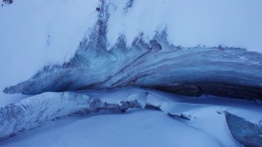 A huge ice wall from a glacier in the mountains. Everything is covered with snow and large stones. Top view from the drone on the cracks in the ice. The glacier breaks, the ice flakes off. Almaty