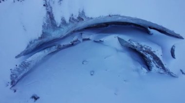 A huge ice wall from a glacier in the mountains. Everything is covered with snow and large stones. Top view from the drone on the cracks in the ice. The glacier breaks, the ice flakes off. Almaty