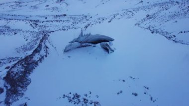 A huge ice wall from a glacier in the mountains. Everything is covered with snow and large stones. Top view from the drone on the cracks in the ice. The glacier breaks, the ice flakes off. Almaty