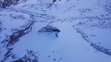 A huge ice wall from a glacier in the mountains. Everything is covered with snow and large stones. Top view from the drone on the cracks in the ice. The glacier breaks, the ice flakes off. Almaty