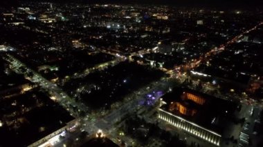 Gece şehrinde büyük bir konser. Kalabalığın insansız görüntüsü, ışınları ve ışık huzmeleri. Işıklı büyük bir bina. Arabalı yollar, yayalı sokaklar ve etrafta bir park var.