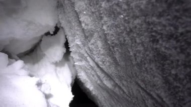 A large ice cave covered with white snow. Grains of white snow like ice stuck to the wall and shine from the light of the lantern. There is only darkness in the distance. A very deep cave in glacier