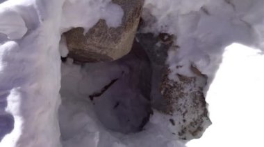 Buzulların ve kayaların altındaki buz mağarasının girişi. Beyaz kar var, deliğin etrafında büyük taşlar. İzler aşağı gidiyor. Buzulun altındaki mağaranın girişi. Kazakistan Dağları