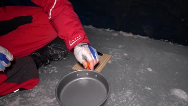 一个家伙在冰洞里用汽油做饭 登山者点燃燃烧器 切香肠和西红柿 把鸡蛋打破 放在煎锅里煎 从食物中提取的蒸汽 冰墙是蓝色的 地面是灰色的 — 图库视频影像