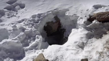 Buzulların ve kayaların altındaki buz mağarasının girişi. Beyaz kar var, deliğin etrafında büyük taşlar. İzler aşağı gidiyor. Buzulun altındaki mağaranın girişi. Kazakistan Dağları