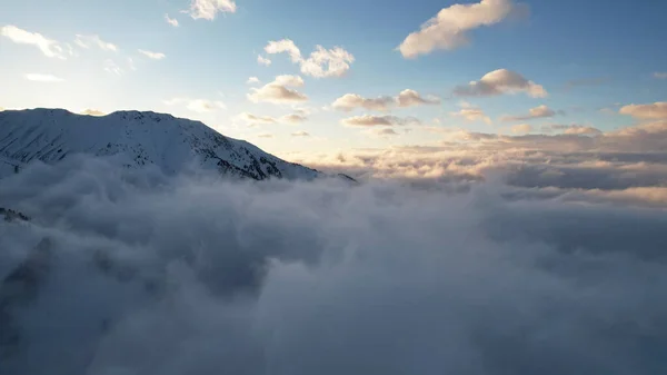 在群山的云海中飞翔 雾就像大海的巨浪冲击着被雪覆盖的高山 云杉生长在一些地方 日落了阳光的橙色光芒 — 图库照片