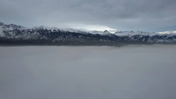 Flying a drone among the clouds with a view of the mountains. The light yellow rays of the sun at sunset are reflected on the surface of the clouds. Double layer of clouds. Mountains are visible