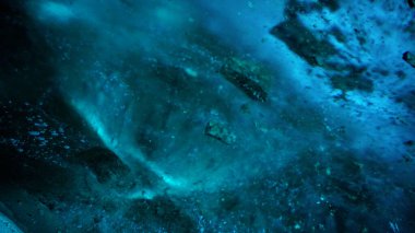 Turquoise pure color of ice inside the ice cave. Stones and icicles are visible in places. Light grains of snow on the ice walls. Frozen air bubbles in an ice wall. An ancient glacier. Color gradient