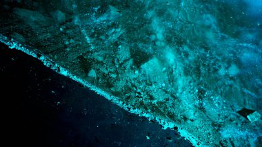 Turquoise pure color of ice inside the ice cave. Stones and icicles are visible in places. Light grains of snow on the ice walls. Frozen air bubbles in an ice wall. An ancient glacier. Color gradient