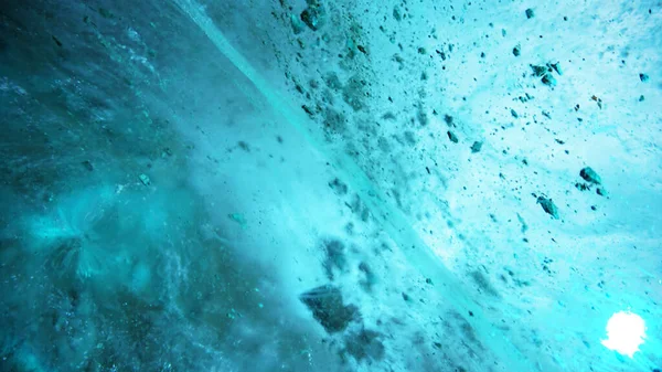 Turquoise pure color of ice inside the ice cave. Stones and icicles are visible in places. Light grains of snow on the ice walls. Frozen air bubbles in an ice wall. An ancient glacier. Color gradient