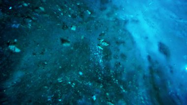 Turquoise pure color of ice inside the ice cave. Stones and icicles are visible in places. Light grains of snow on the ice walls. Frozen air bubbles in an ice wall. An ancient glacier. Color gradient