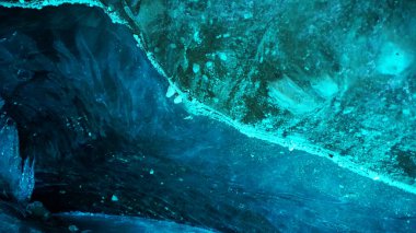 Turquoise pure color of ice inside the ice cave. Stones and icicles are visible in places. Light grains of snow on the ice walls. Frozen air bubbles in an ice wall. An ancient glacier. Color gradient