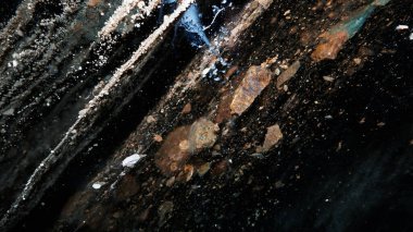 The black transparent color of ice in the cave. Small stones hang down in places. There are frozen air bubbles and grains of sand in the ice. Black-brown shade of ice. Deep in the glacier. Epic