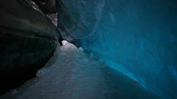 A huge corridor inside an ice cave in the mountains. The turquoise color of the ice gives a special atmosphere. There is snow on the icy floor. Clean walls of ice let in light. Tons of ice.