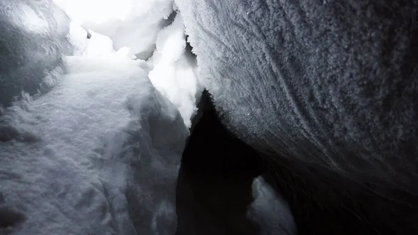 A large ice cave covered with white snow. Grains of white snow like ice stuck to the wall and shine from the light of the lantern. There is only darkness in the distance. A very deep cave in glacier