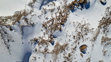 A huge frozen glacier in the mountains and a lot of tourists. Walking in the snow, taking photos with ice. Top view from a drone. Ice resembles marble. Dark light gray tones. Snowy mountains. Almaty