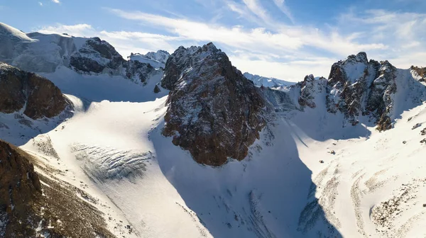 高い雪の氷河の間で山のキャップ 岩の多い峡谷の無人機からの空中ビュー 氷河は雪と岩で覆われている 空は青く 太陽は明るく輝いている 氷が割れてる — ストック写真