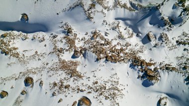 A huge frozen glacier in the mountains and a lot of tourists. Walking in the snow, taking photos with ice. Top view from a drone. Ice resembles marble. Dark light gray tones. Snowy mountains. Almaty