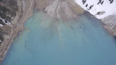 Dağlarda turkuaz mavi suyu olan bir göl. Temiz su, kozalaklı ağaçlar ve karlı dağlar. İnsanlar kıyı boyunca yürür, alçak çalılar büyür. Büyük Almaty Gölü. Kazakistan