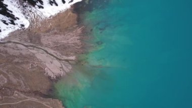 Dağlarda turkuaz mavi suyu olan bir göl. Temiz su, kozalaklı ağaçlar ve karlı dağlar. İnsanlar kıyı boyunca yürür, alçak çalılar büyür. Büyük Almaty Gölü. Kazakistan