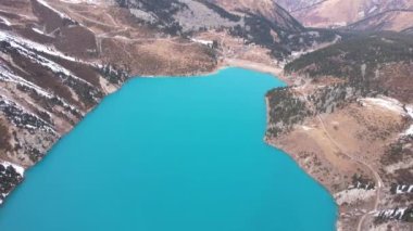 Dağlarda turkuaz mavi suyu olan bir göl. Temiz su, kozalaklı ağaçlar ve karlı dağlar. İnsanlar kıyı boyunca yürür, alçak çalılar büyür. Büyük Almaty Gölü. Kazakistan