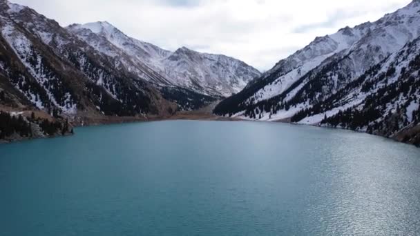 山中的一个湖 深蓝色的水 俯瞰湖面 太阳光 针叶树和雪山 远处有一个峡谷 岸上长出低矮的灌木丛 — 图库视频影像