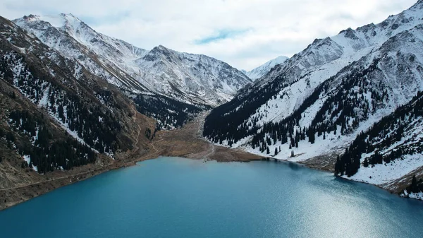 stock image A lake in the mountains with turquoise blue water. Drone view of clear water, coniferous trees and snowy mountains. People walk along the shore, low bushes grow. Big Almaty lake. Kazakhstan