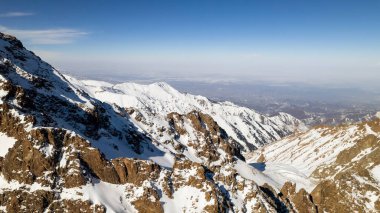 High snow-capped mountains among glaciers. Aerial view from a drone on a rocky gorge. The glacier is covered with snow and rocks. The sky is blue and the sun is shining brightly. The ice is cracking