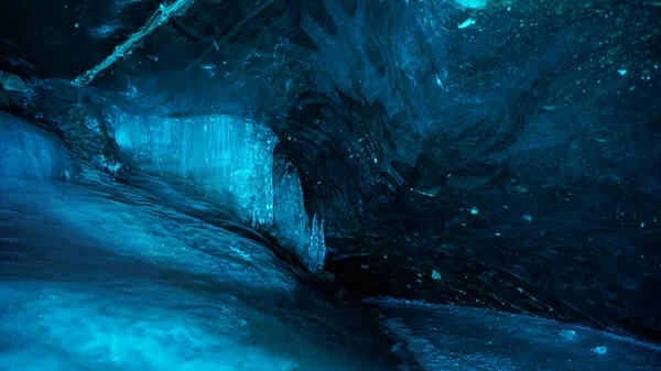Turquoise pure color of ice inside the ice cave. Stones and icicles are visible in places. Light grains of snow on the ice walls. Frozen air bubbles in an ice wall. An ancient glacier. Color gradient