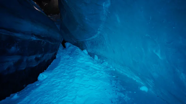 A huge corridor inside an ice cave in the mountains. The turquoise color of the ice gives a special atmosphere. There is snow on the icy floor. Clean walls of ice let in light. Tons of ice.