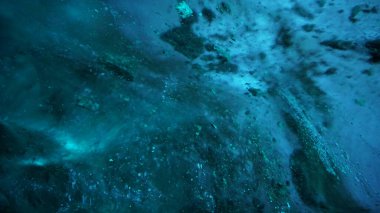 Turquoise pure color of ice inside the ice cave. Stones and icicles are visible in places. Light grains of snow on the ice walls. Frozen air bubbles in an ice wall. An ancient glacier. Color gradient